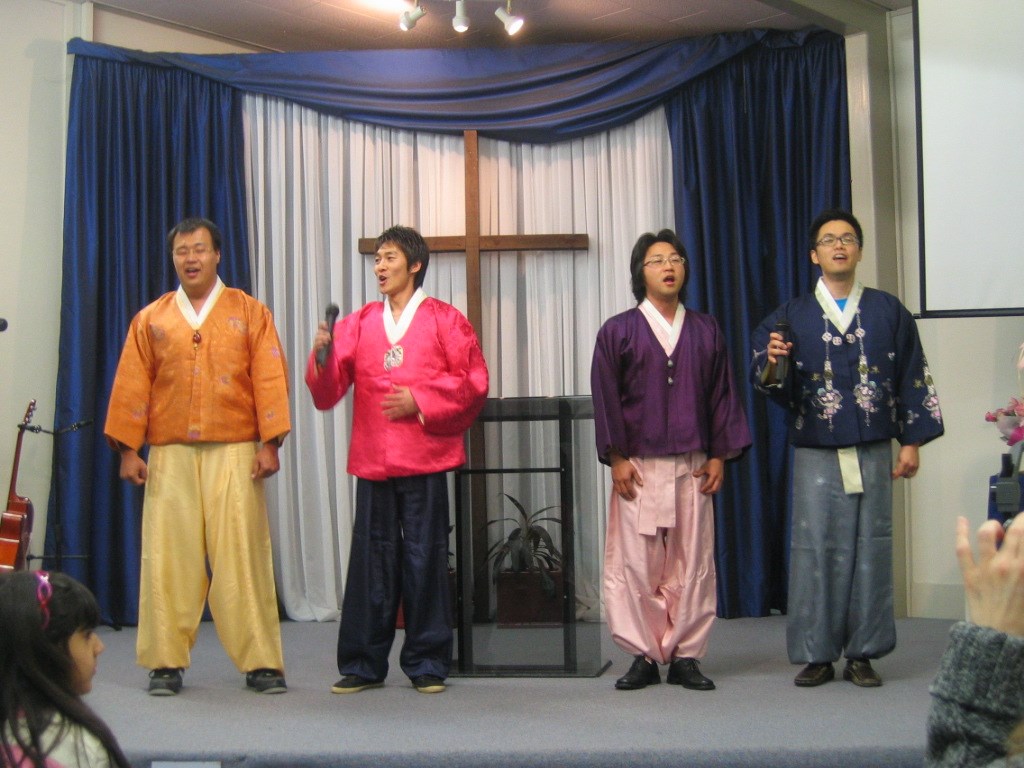 A group of Korean men in traditional attire singing on stage.