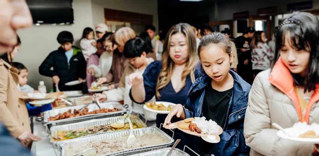 A group of people waiting in line and taking food on the banquet table