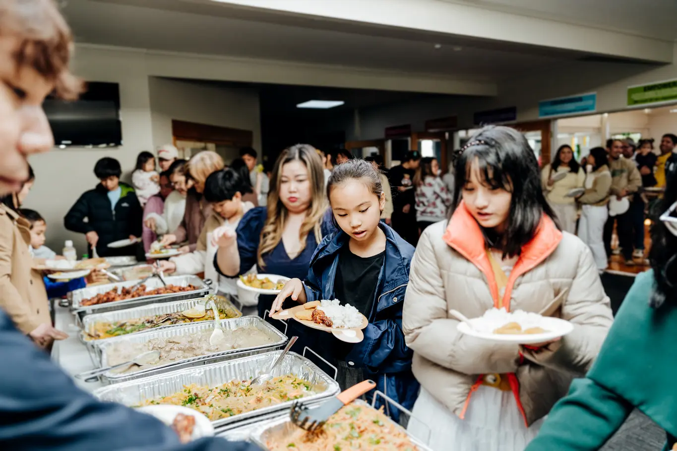 A group of people waiting in line and taking food on the banquet table