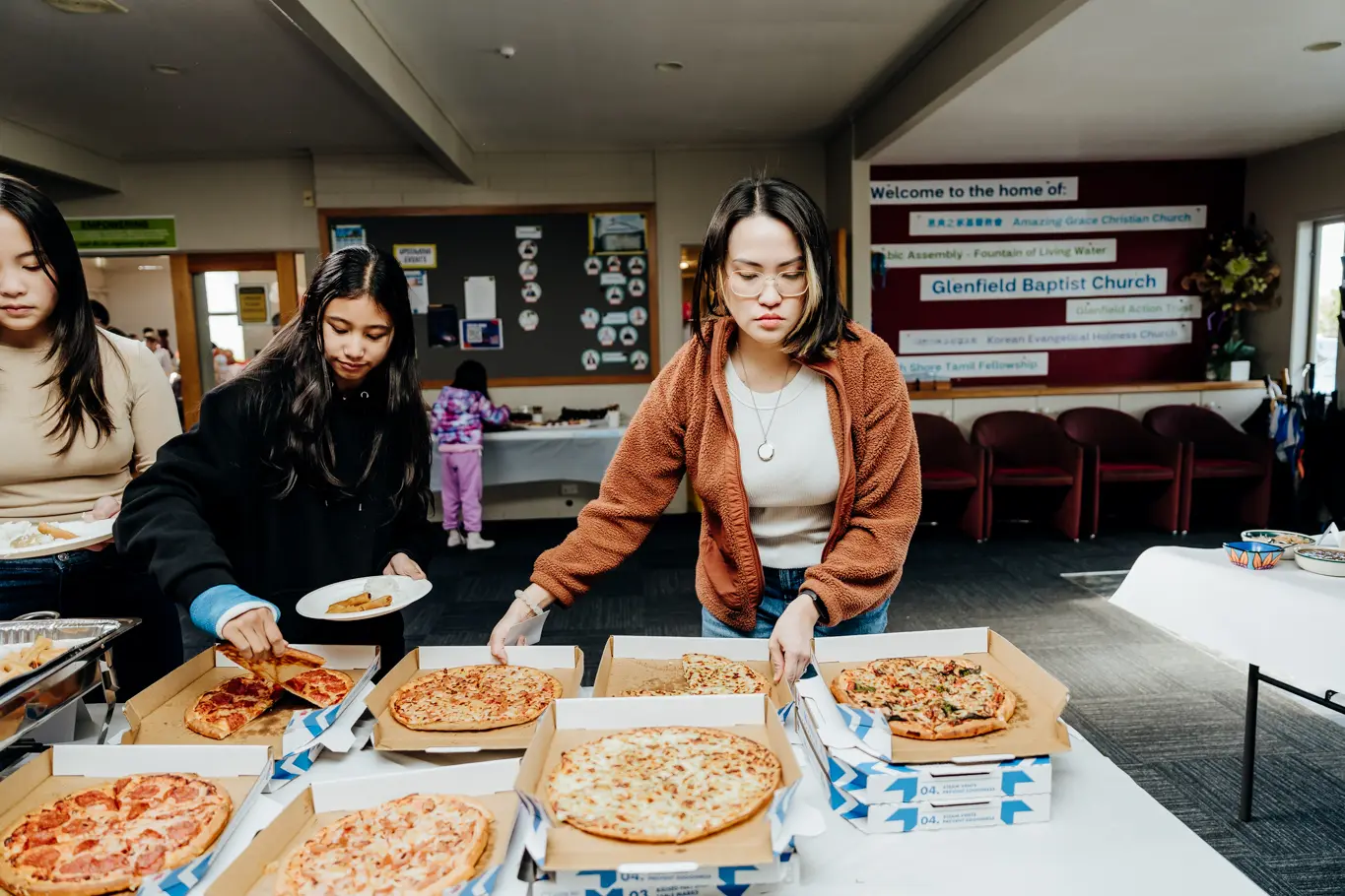 A photo of three women taking pizza on their plate on a banquet food table.