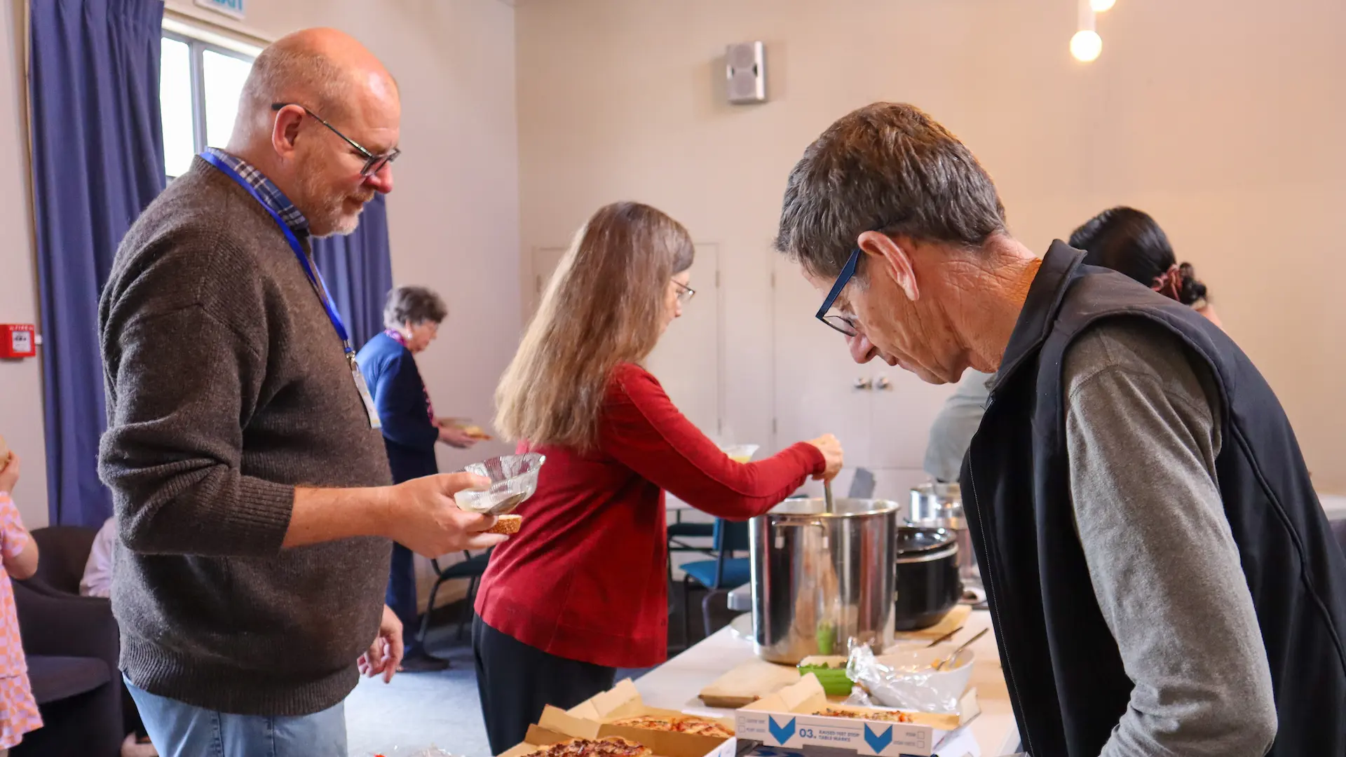 Various people conversing and getting food at a banquet table during Glenfield Baptist Church's shared lunch events.