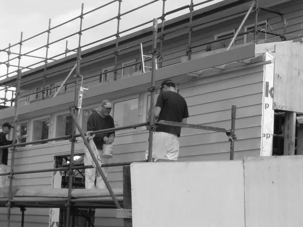 A black-and-white photo of two men on scaffolding, building part of the church.