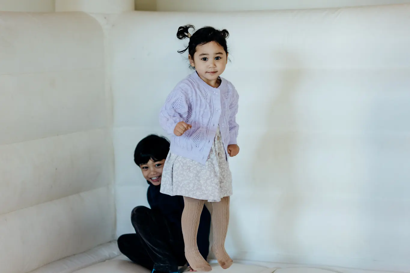 A young Filipino toddler jumping in a white bouncy castle.
