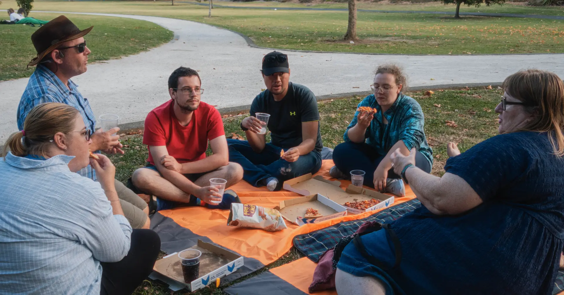 A group of people conversing, sitting down while having a picnic in the park.