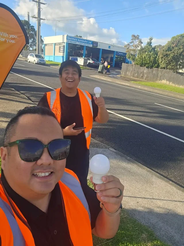 Two Filipino men in traffic vests holding a lightbulb and smiling as they take a selfie